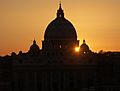 The dark silhouette of St. Peter's dome set against the orange, evening sky and setting sun.