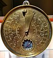 Circular brass time measurement device with engraved Arabic toponyms and zodiac symbols.