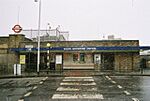 A brown-bricked building with a rectangular, dark blue sign reading "SOUTH WOODFORD STATION" in white letters all surrounded by snowflakes