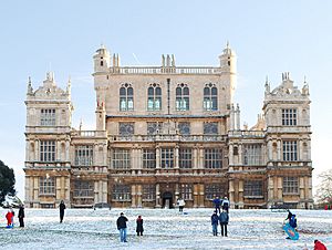 Tall, decorated sandstone building with a clear sky behind and people and snow on the ground in the foreground.