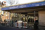 A grey building with a blue sign reading "BERMONDSEY STATION" in white letters and four bicycles lying idle in the foreground all under a blue sky