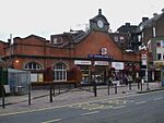 A brown-bricked building with a rectangular, blue sign reading "HAMMERSMITH STATION" in white letters all under a grey sky