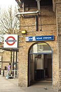 A beige-bricked building with a dark-blue, rectangular sign reading "LATIMER ROAD STATION" in white letters all under a white sky