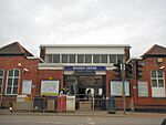 A brown-bricked building with a rectangular, dark blue sign reading "NEASDEN STATION" in white letters all under a light blue sky with white clouds