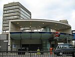 A grey building with a rectangular, dark blue sign reading "SOUTHWARK STATION" in white letters all under a light blue sky with white clouds