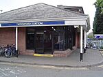 A red-bricked building with a rectangular, dark blue sign reading "WOODFORD STATION" in white letters all under a clear, white sky