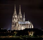 A large, brightly lit cathedral sits in the middle of a skyline at night.