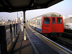 A grey, red and blue A Stock Stock East London Line train waiting to depart New Cross Station for Whitechapel.