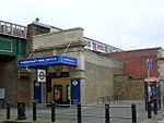 A brown-bricked building with a rectangular, dark blue sign reading "RANVENSCOURT PARK STATION" in white letters all under a blue sky