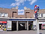 A brown-bricked building with a rectangular, light blue sign reading "METROPOLITAN & PICCADILLY LINES" in white letters all under a blue sky