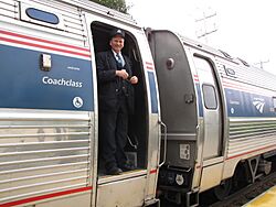 An Amtrak conductor standing in the doorway of an Amfleet cars with its trapdoor in the closed position