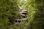 A house with a waterfall going through, surrounded by a forest