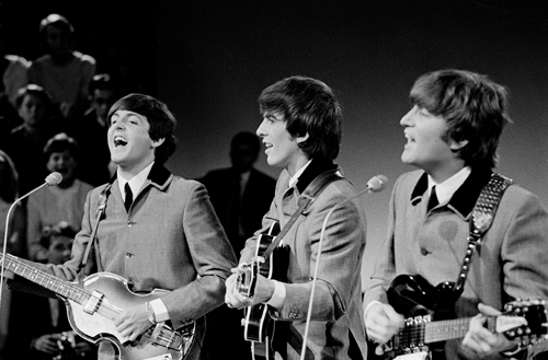 Paul McCartney, George Harrison, och John Lennon spelar gitarrer och bär matchande grå kostymer.