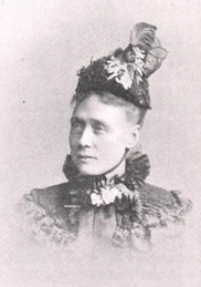 A white woman wearing a tall, elaborate bonnet and a high-collared capelet, fastened at the throat.