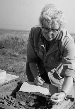 Margaret Ursula Jones, shown filling in a form on a clipboard whilst inspecting freshly-excavated potsherds on site at Mucking.