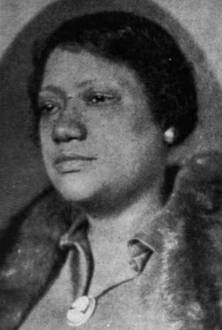 A Black woman wearing a fur stole over a dress with a collar, and a cameo pinned to the front