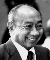 Black and white photograph of the head and shoulders of a balding Chinese man in a suit and tie, smiling handsomely