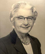 Black and white portrait photograph of Berth Swirles take in 1962. She is wear a jacket, blouse, a necklaces and spectacles. She is smiling.