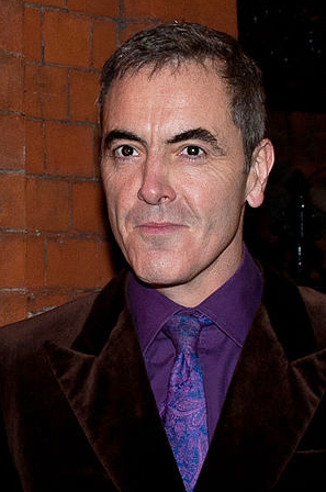 A man wears a purple shirt, a patterned tie, and a black jacket.