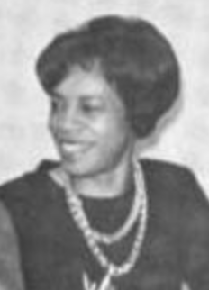 A smiling Black woman with a short bouffant hairstyle, wearing a dark dress with two strands of beads