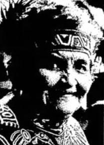 An older Tlingit woman, wearing a headband and robe with embroidered motifs