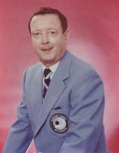 Middle-aged man wearing a light blue suit jacket with a CBC Sports crest