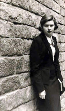 Black and white photograph of a young woman leaning against a brick wall.
