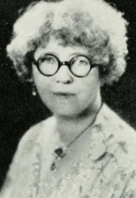 Portrait of an older white woman with curly grey hair, wearing round glasses.