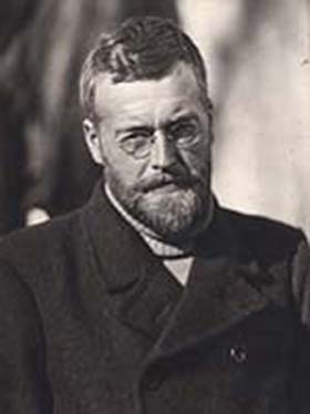 Black and white photograph of James Wordie. He is wearing spectacles, has a beard and is wearing a heavy overcoat and rollneck jersey.
