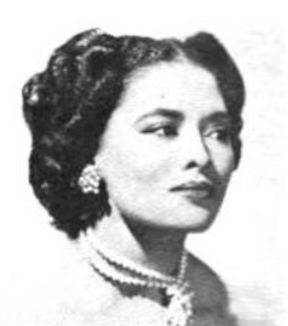 A light-skinned woman with coiffed curly dark hair and glamor makeup, wearing pearls