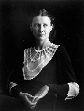 Portrait in black and white of woman in black dress with a large white bodice, lit from the right, against a black background.