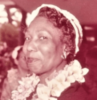 a 3/4 shot of a woman smiling at the camera, the image is balck and white, with a pink tinge. The woman is wearing a lei