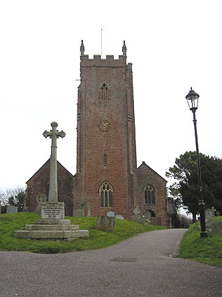 Reddish stone building with square tower. In the foreground are a cross and lamppost.