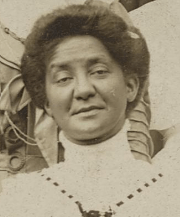 A middle-aged African-American woman, from a 1909 photograph; her hair is dressed in a bouffant updo, and she is wearing a high-collared white lace blouse with a ribbon detail.