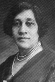 A middle-aged African-American woman, hair cropped to chin length, wearing a dress with a surplice neckline and pearls