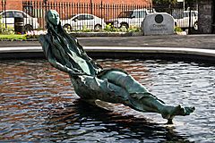 Bronze sculpture of a young woman reclining with legs crossed, in a pool of water