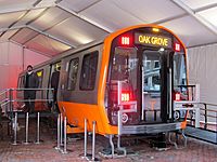 A subway rail car prototype with orange trim sits on a raised platform a tent with stairs to one entrance and a ramp to the opposite entrance