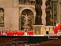 The cardinals, all in bright red robes, are grouped near the baldachin.