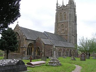 Gray stone building with ornate square tower and slate roof. In the foreground are gravestones