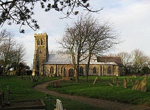 A stone church seen from the south, with a slightly leaning west tower on the left, a long south aisle to the right, and a porch