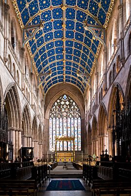 Interior of nave with blue vaulted ceiling with gold stars. A very complex east window