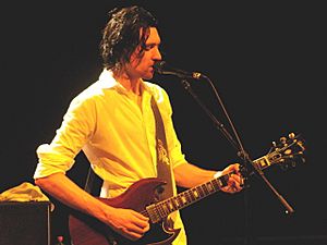 A thirty-year-old man is playing a six-string electric guitar while singing into a microphone.