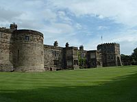 A two-storey castle with a two-storey circular tower on the left and a three-storey octagonal tower on the right. The castle overlooks a green lawn.
