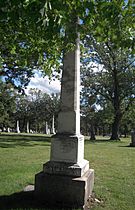 A white grave column worn by weather set among trees.