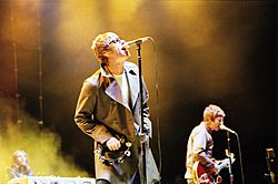 Oasis performing live. From left to right: Jay Darlington (background), Liam Gallagher, Noel Gallagher.