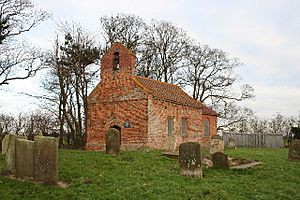 A small, simple brick church seen from the southwest in a churchyard, with a single bellcote at the west end