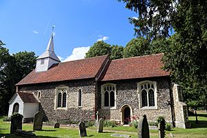 A flint church with red tiled roofs and a white wooden spire