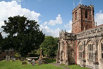 Stone building with square tower. In the foreground are stone crosses, gravestones and trees.