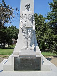 Granite statue of a young soldier in military uniform standing in front of an obelisk atop a plaque describing his achievements