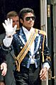 Michael Jackson, an African-American musician in his mid-20s wearing a sequined army style jacket and black sunglasses. He waves his right hand, which is adorned with a white glove.